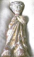An earthenware figure of a tall thin woman dressed in sumptous robes that she has gathered in her left hand, her hair coiffed high upon her head. &nbsp;It is covered in a white slip with traces of polychrome mineral pigment.