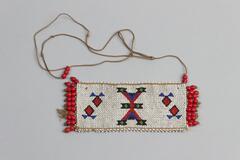 Beaded jewlery with a rectangular piece with a red beaded fringe on two sides. White small beads with geometric pattern in red, black, blue and green. Long brown string coming off one end with beaded end. White tag attached.