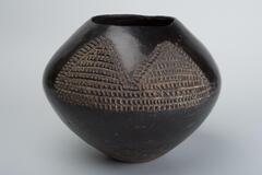 Black pot that is widest at the middle with etched triangular designs on two sides.