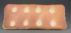 A rectangular shaped plate with eight circular patterns. The rim is slightly flared out to create the concave shape. The top surface is unglazed, scorched to an intense red. The bottom does not have foot. In the kiln, the thick clay slabs were stacked close together so that the floating ash landed on the edge of the plate facing the flame. The circular patterns are areas that were protected from the flame by cylinder clay spacers.