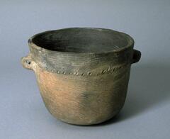 A nearly cylindrical, dark gray and brown earthenware pot, with somewhat larger diameter at top than bottom and small, knob-like handles on either side near the top. Decorated wtih a line of small circular indentations around the upper portion, in line with the handles. Coarse linear imprints cover the entirety of the pot.