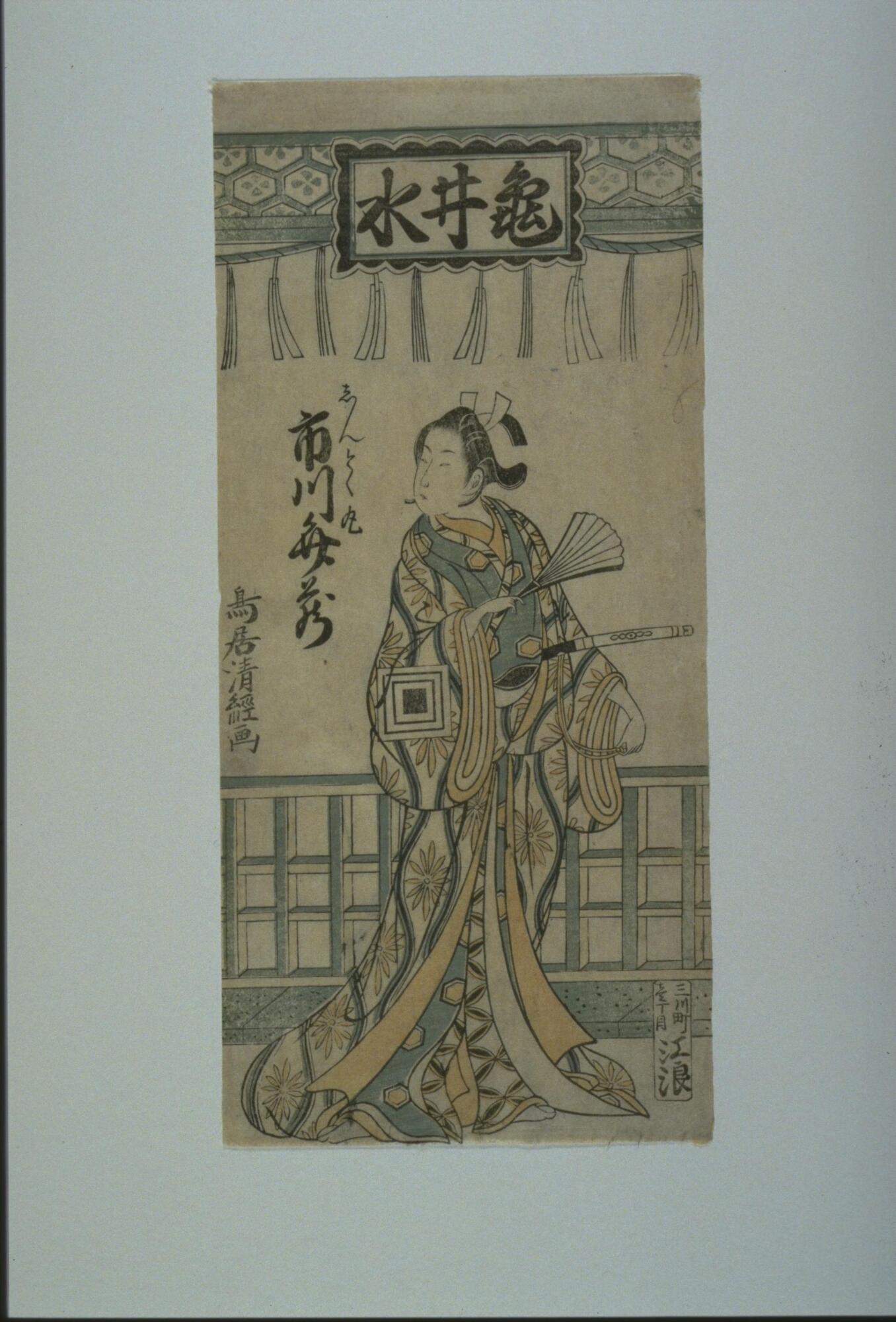 A man dressed as a woman stands under a blue and white fringed drape that reads <em>Kamei no mizu</em>. The man is wearing a orange, blue, and black multi-layered robe with floral bursts on the outer layer. He carries a sword in his belt and holds an open fan in his right hand. His hair is tied back with a white ribbon. He is standing in front of a fence or lattice.<br /><br />
Inscriptions: Ichikawa Benzō, Shintokumaru; Mikawachō [?] chō me, Enami (Publisher's seal); Torii Kiyotsune (Signature)
