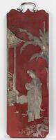Red lacquered panel with a mother-of-pearl inlay creating the image of a tree, two women and the exterior corner of a structure. There is a metal hinge on the top. 
