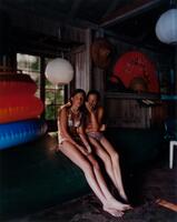 This image is the far right panel of a triptych and depicts an interior view of a dark cabin. Two young girls in swim suits are sitting inside and behind them stands a stack of inflatable tubes.