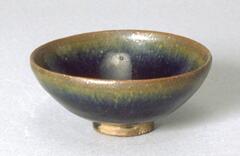 Round base bowl on a tall straight foot ring, covered in a dark brown-black glaze with subtle hare's fur markings (兔毫盏 <em>tuhao zhan</em>).