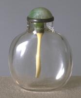 A round clear glass snuff bottle. On top of the bottle is a jadeite stopper.