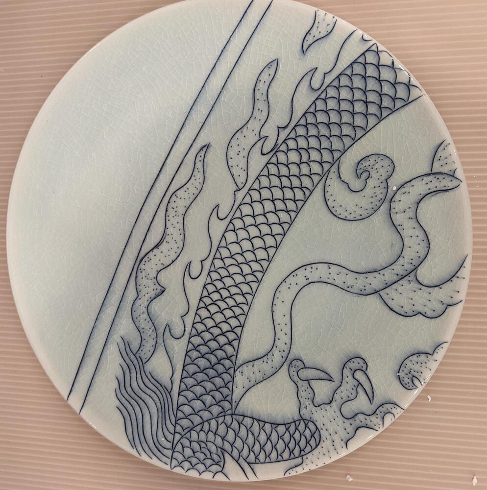 A plate from the border of the piece. Two thin blue lines descend from the center top to the lower left of the piece. To the right of the lines is a portion of a dragon&#39;s scaly body, leg, and claws.