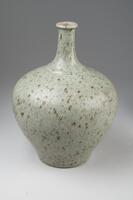 A tall vase with a narrow neck and broad top, where it flattens out and a tall narrow neck extends with a narrow mouth. Piece is blue-green ceramic with black and brown specks.