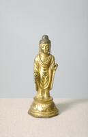 Gilt bronze standing Buddha on lotus pedestal. He is clothed in monastic robes with cascading U-shaped folds, similar to the gentle folds of his neck. His hands ake the form of two mudras: the abhaya (&ldquo;have no fear&rdquo;) mudra with the right hand, and varada (&ldquo;wishes are granted&rdquo;) mudra with the left.<br />
<br />
<br />
It is well proportioned overall and represent Buddha in a standing position; a position quite popular in Unified Shilla Buddhist sculpture. The Ushinisha on the top of Buddha&#39;s head is tall, voluminous and black. The face is plump and facial features, including the eyes, nose and the mouth, are all rather small. The earlobes hang are hanging and the three curved lines on the neck are highly distinct.<br />
<br />
The body and pedestal of this statue were cast as a single mass. The body is made of solid bronze, but the pedestal is hollow. The back part of the pedestal features a hole for the insertion of a mandorla, which is missing. Unlike most Buddha statues from