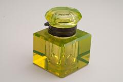 This is a yellow cut crystal inkwell with a metal collar. The body is a cube shape with cut corners and the round cap has a multifaceted surface.<br />
