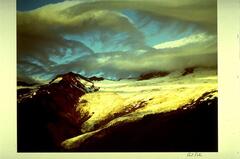 This photograph depicts a view of a snow-capped mountain with clouds grazing its surface.