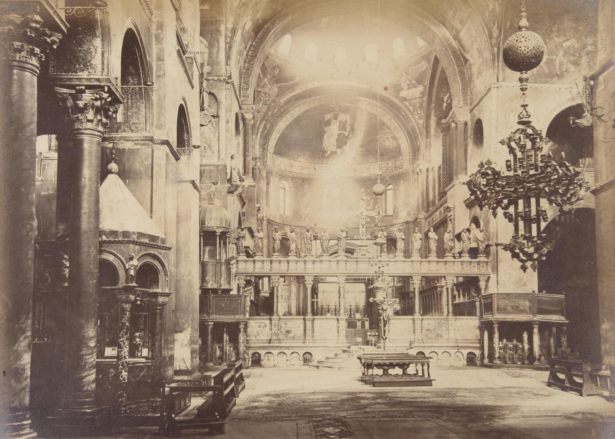 This photograph depicts a view of a church interior looking towards the high altar. In the walls and dome of the chapel are windows through which sunlight shines.