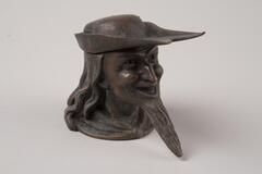 A copper inkwell in the shape of a man's head with a long, pointed beard.  His hat acts as the stopper.