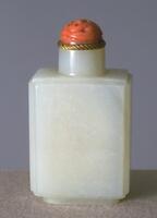 A white jadeite snuff bottle that is rectangular, is on a footing, and has circular neck with a gold rim and ends with a pink stopper.