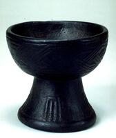 Circular bowl-shaped cup with black base. Linear vertical carvings are on the base and interlocking lines are wrapped around the bowl portion. 