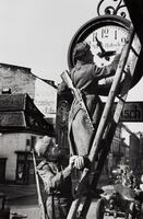Two soldiers stand on, and near a ladder and adjust an outdoor clock which overhangs a town street.