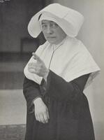 A nun wearing a habit with her left hand pointed. She is looking at the camera.