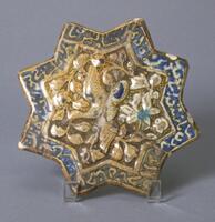 <br />
This Ilkhanid eight-pointed star tile employs the Kashan style that originates in Iran. A crane/phoenix-type bird flies amongst floral decorations. The outer perimeter is decorated with a cursive script. The script may either be Qur'anic verse (Arabic) or a Shahnama verse (Persian book of Kings). (updated)