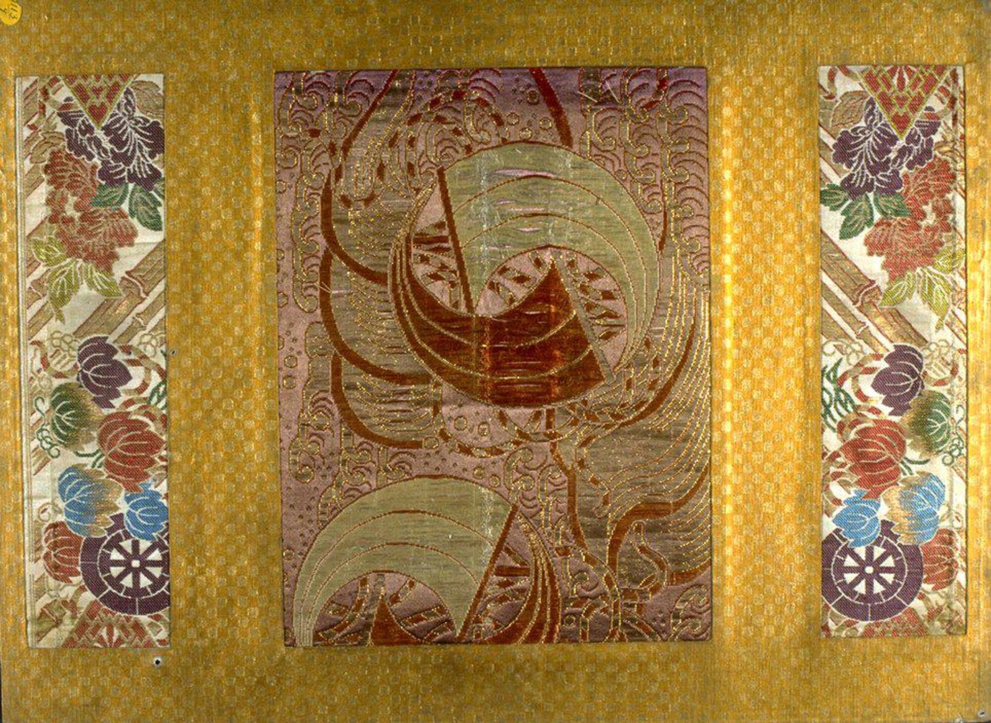 The colorful strips of brocade at the top and bottom of this panel feature a woven design of ivy and peonies entwined around cartwheels, bamboo, and stylized diamonds. A wide rectangular fragment of an obi (sash for kimono) lie at the center of the textile. It is an almost abstract design of boats tossed in a frothy sea. The warm, muted tones of the gold are matched in color selections of mauve, and muted purple, blue, and green threads.