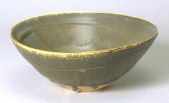 Stoneware teabowl with dark green glaze coating the inside and outer top three-quarters of the dently curving sides.  The green glaze drips off the side of the bowl near the base, frozen in suspension.  At the rim of the bowl the color of the stoneware shows through a thin layer of glaze.