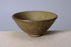 A conical bowl on a tall straight foot ring, covered in a thick olive-brown mottled glaze. The too-thick glaze is crawling away from the underlying clay body in a crackle pattern.