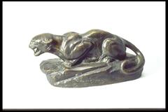 This bronze sculpture represents a leopard. On a rocky outcrop, the animal is in a crouching position with its mouth slightly open. Its tail curls down by its hind leg, next to which the work is signed, inscribed in the clay model, "Edward S. Kemeys."