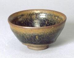 This conical bowl on a tall straight foot ring is covered in a dark brown-black glaze with subtle hare's fur <em>兔毫盏 (tuhao zhan)</em> markings. 