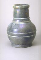 Ceramic vessel with rounded body, long thick neck and wide lip. Two decorative bands encircle the body of the vessel and two encircle the neck near the shoulder. Vessel is covered with mottled iridescent glaze in shades of dark blue.