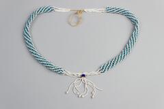 Blue and white beaded necklace with darker blue bead and white tassle at bottom. Loose white bead from tassle. White tag attached.