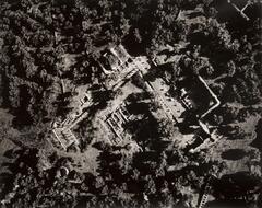 This photograph depicts an aerial view of ruins and the surrounding archaeological sites on a bright day with shadows cast by trees.