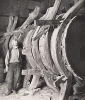 A man standing next to a large wooden barrel. The barrel appears to be hand constructed.