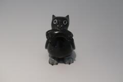 A hawk carved from smooth black stone with prominent ears and eyes and unpolished feet. It holds a small lemming in its mouth.