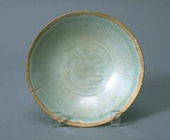 A thin porcelain conical bowl with a direct rim on a footring.  The interior has incised double fish decorations and six linear divisions around the walls.  It is covered in a white glaze with a bluish tinge, and an unglazed rim.