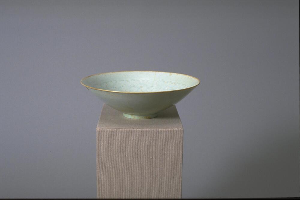 This thin porcelain conical bowl with direct rim on a footring has an interior with incised and combed floral or cloud-like meander decoration. It is covered in a white glaze with bluish tinge, and it has an unglazed rim.