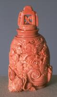 A coral snuff bottle with dragons among the clouds. On top is a coral stopper.