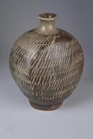 A jar with rectangular shaped body and a narrow neck opening. It has lines and strokes of black patterns on the outer body of the jar. Body rope mishima imprint in rows. Tan and brown matte glaze.
