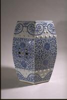 A blue and white garden stool decorated with floral patterns. Square and oval pieces are cut from the sides.
