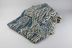 A blue and off-white tunic in a square shape. The tunic is decorated with various geometric designs sewn together. 