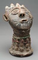 This terracotta head with a striated neck is decorated with a pattern of raised knobs and two strings of multi-colored beads. The base of the neck is decorated with three rings of wavy lines. The face is somewhat flat and circular, tilting backwards slightly. There are three diagonal marks on each side of the open mouth. The eyes are almond shaped, framed by brows in the form of one curved line. The hairstyle is formed by four triangular projections. The oblong-shaped ears sit high on each side of the face. 