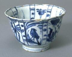 A small, thin, porcelain bowl with an everted, foliate rim, on a foot ring.  It is painted in an underglaze blue decoration of birds and flowers, separated into eight panels on both the interior and exterior, and covered in a clear glaze. 