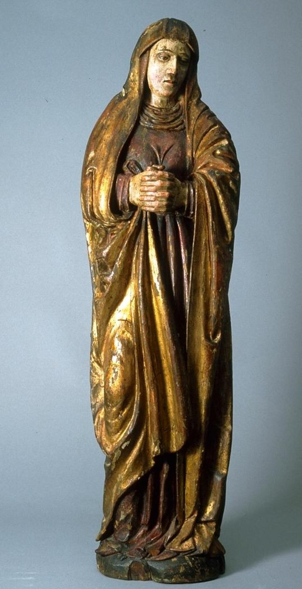 This standing figure of the Virgin turns slightly toward the left with her head bowed and hands clasped before her in a restrained expression of grief. Her robe is gilded, which contributes a regal note to this somber figure.