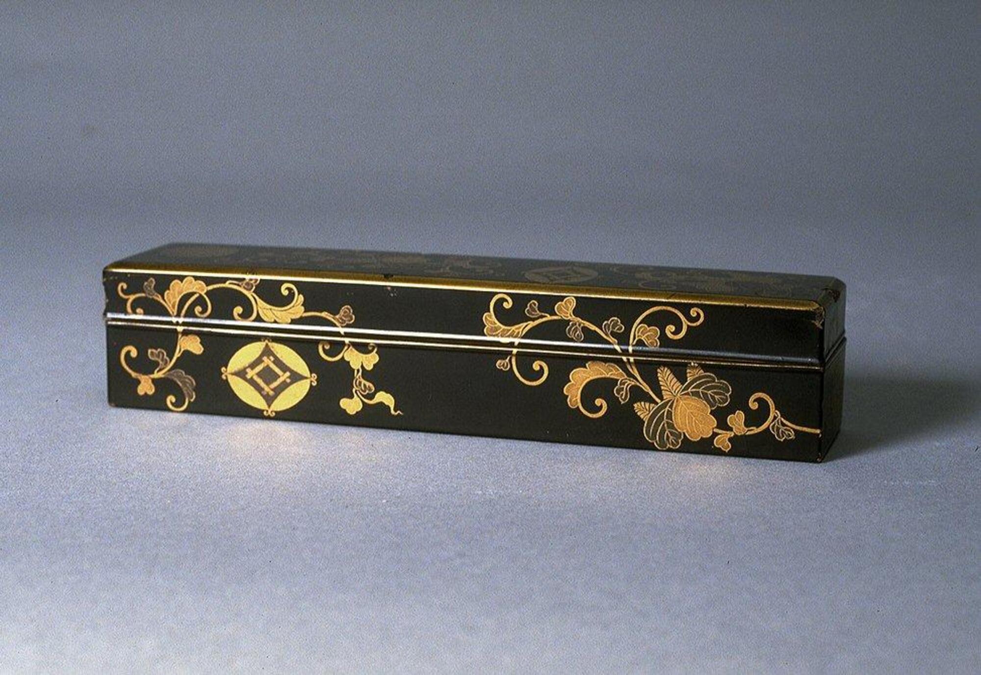 The long rectangular box is covered with an intricate floral pattern of gold on a black background in lacquer. Two house crests (one a geometric representation of a well and the other a chrysanthemum flower) appear in the design. Part of a bridal trousseau.