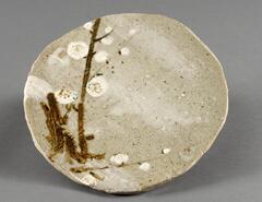 It is a round, stoneware plate. Clay is red covered with mottled grayish glaze and painted with underglaze iron and white slip. Imperfection of clay was resulted in occasional bumps on surface. Six spur marks are visible on the bottom. Slab is roughly cut (deliberately); the plate is in slightly convex shape. Artist’s seal with underglaze iron appears on the bottom.