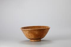 This porcelain bowl was produced at a regional kiln in the regions of Gimhae-si, Jinhae-si, Jinju-si, Sacheon-si, and Gonmyeong-myeon in southwestern region of Gyeongsangnamdo in the 16th century, Joseon. Such bowls were known to the Japanese as &ldquo;ido (井戶)&rdquo; tea bowls and treated as luxury items. Though this bowl was intended to be made as a white porcelain bowl, the numerous impurities stuck to its surface tinged the surface with brown. Refractory spur marks remain on the inner base and the foot. There is a large number of pinholes on the foot and lower part of the wall, and impurities stuck inside the pinholes appear like dotted decoration. There are traces of glaze running, some of which were caused by melting and flowing down. Although this was previously classified as a Japanese artifact, it is thought to have been produced in Korea and later used in Japan as a tea bowl. Therefore, the Overseas Korean Cultural Heritage Foundation newly added this bowl as a Korean object after a careful examinat