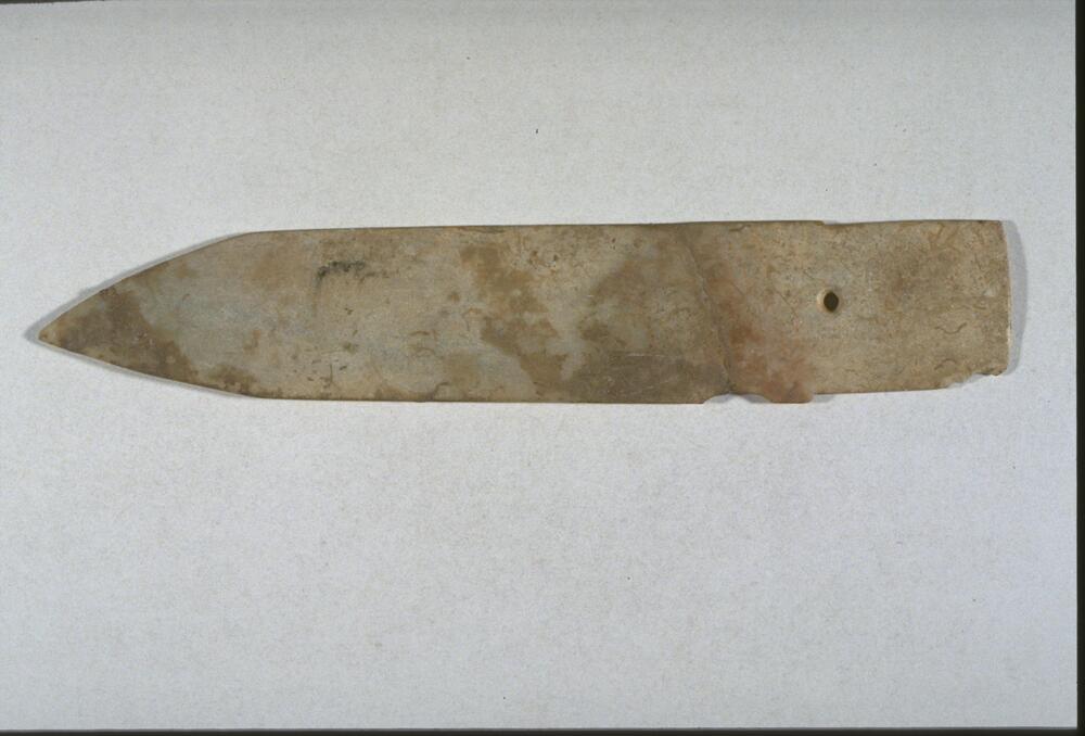 ceremonial jade ge dagger-axe, pointed blade on one end and squared tang for hafting on the other. It was broken and mented in the middle. Traces of cinnabar, red mercury sulfide, remain on the jade surface, indicating it probably came from a Shang elite burial in China. The jade material was probably fire treated to create the bony look.  <br />