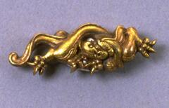 Golden lion with gently curving tail and arched back.  Each foot is capped with three intimidating claw-like nails.  The lion is oriented as if stalking from left to right, but the head turns back inward towards the center, with a downward flowing mane.