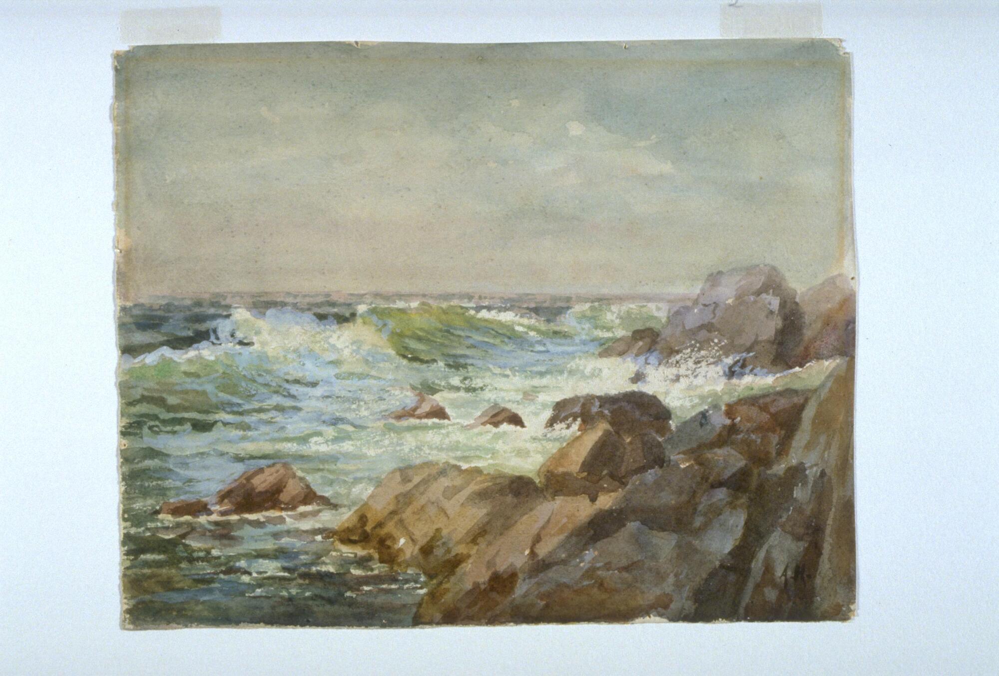 Waves crashing on the rocks which are mostly situated on the right bottom half of the image. The sky is gray and blue while the water is a mix of greens, blues and white.