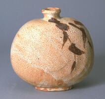 Flask-shaped bottle with short, narrow neck. Bamboo leaves design in brown color is applied on one shoulder toward the bottom. The porous surface of white glaze shows the orange color of the clay. The spout is narrow and has an elevated rim. The foot is short and glazed.