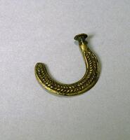 Flat piece of brass in a semi-circular shape with a round flat end and a raised braided pattern. 