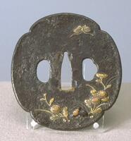 The flat iron plate with quatrefoil design. It has three holes: one for blade (middle) flanked by oval-shape hole (for kougai) and oval with bump shape (for kozuka). Chrysanthemums, autumn grass and a rock are carved on lower-right side; a butterfly is descending toward the flowers. Gold inlays are applied to the flowers, grass, part of the rock, and butterfly. The surface is finely granulated by etching (“ishime-ji”).